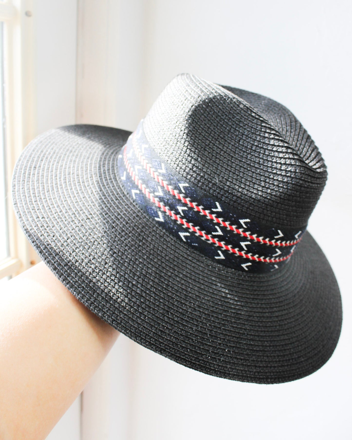 Black straw basket weave wide brim fedora hat with red and blue asymmetrical design strip band around 