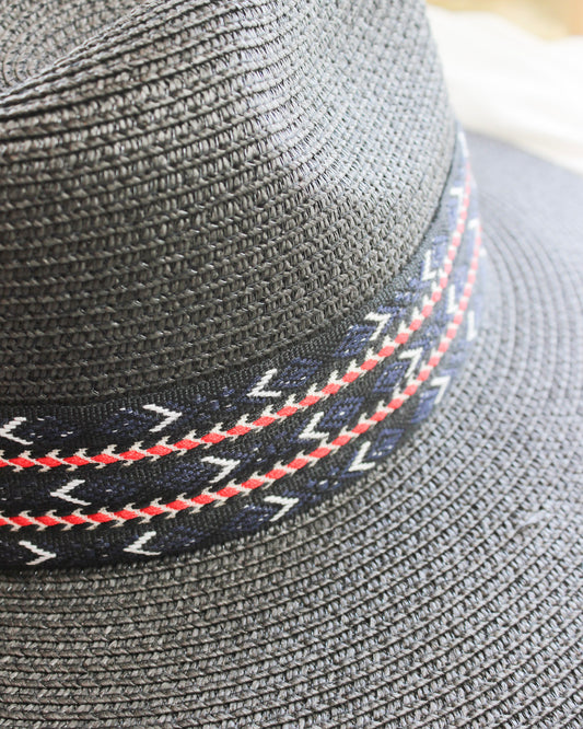 Black straw basket weave wide brim fedora hat with red and blue asymmetrical design strip band around 