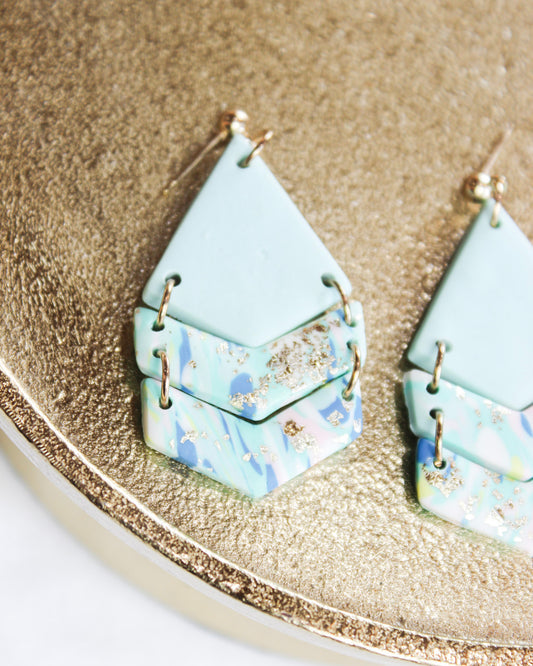 Light baby blue triangle dangle earrings with paint detail on dangles and gold accents